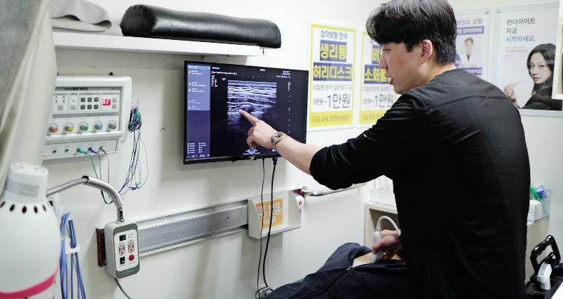 교통사고 환자의 목·어깨를 초음파로 검사하며 화면을 가리키는 장면