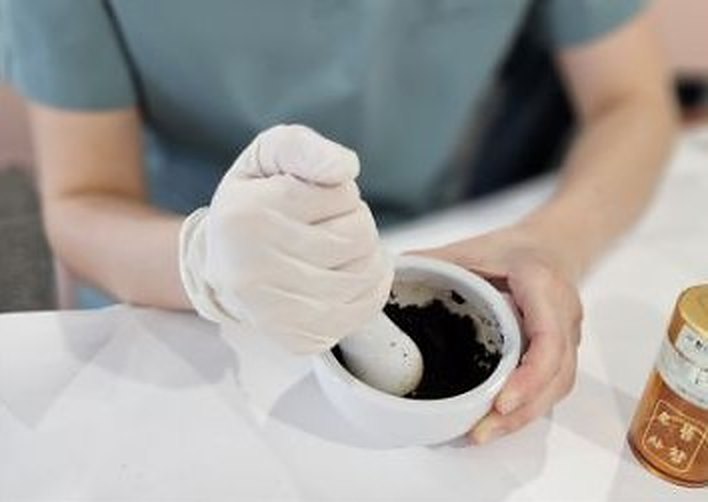 장갑을 낀 손으로 사발에 담긴 공진단 약재 반죽을 고르는 장면